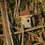 Rifugio per uccelli realizzato con materiali riciclati in un giardino verde e fiorito.